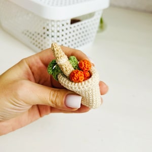 May include: A crocheted cone-shaped basket filled with small crocheted carrots and orange balls. The basket is held in a hand.