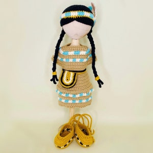 May include: Crocheted doll wearing a brown and blue dress with a yellow and brown belt and matching moccasins.