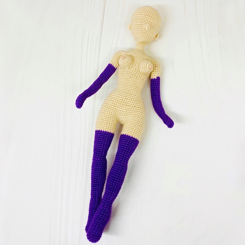 May include: A crocheted doll with a nude body and purple stockings. The doll has a simple face with no features.