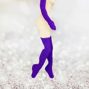 May include: A crocheted doll with a nude body and purple stockings. The doll is standing on a white background.