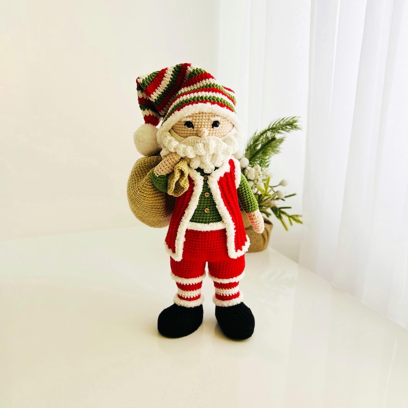 May include: A handmade crochet Santa Claus doll, featuring a red and white striped hat with a white pom-pom, a white beard, and a red vest with white trim. He wears red pants with white stripes and black boots, carrying a beige sack.