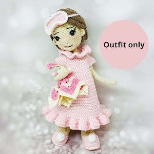 May include: A pink crocheted doll wearing a pink nightgown and a white eye mask. The doll is holding a pink and yellow crocheted blanket. The doll is standing on a white surface. Outfit only.