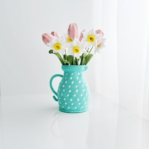 Könnte beinhalten: Ein gehäkelter Strauß aus rosa Tulpen und weißen Narzissen in einem blauen und weißen Tupfenkrug.