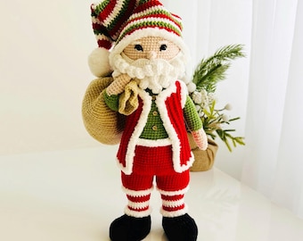 May include: A handmade crochet Santa Claus doll, featuring a red and white striped hat, a white beard, and a red suit with a green shirt. The doll is holding a beige sack and has black boots. A festive Christmas decoration.
