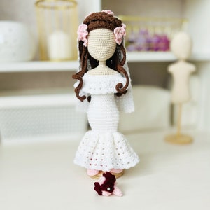 May include: A crocheted bride doll with brown hair, a white dress, and a veil. The doll is holding a small bouquet of flowers.