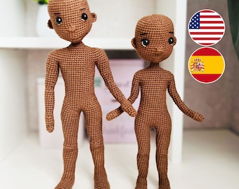 May include: Two crocheted dolls with brown skin and black eyes. The dolls are standing side-by-side on a white surface. The doll on the left is taller than the doll on the right.