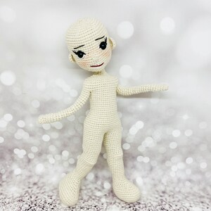 May include: A crocheted doll with a white body and black eyes. The doll has a simple, sweet expression.