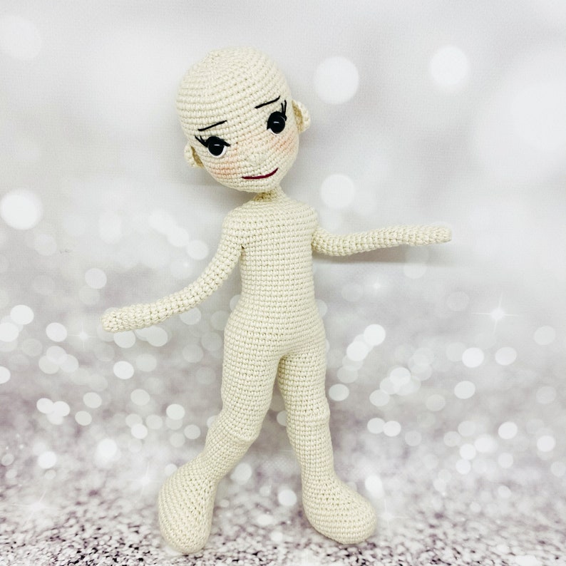 May include: A crocheted doll with a white body and black eyes. The doll has a simple, sweet expression.