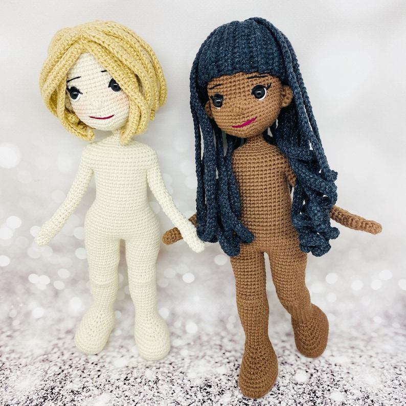 May include: Two crocheted dolls, one with blonde hair and a white outfit, the other with black hair and a brown outfit.