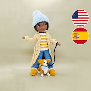 May include: A crocheted doll with brown skin, wearing a blue hat, a beige coat, blue jeans, and holding a leash attached to a crocheted corgi puppy. The doll is standing on a beige background.