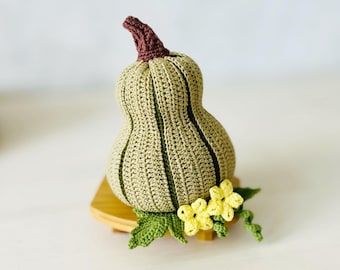 Puede incluir: Una calabaza de ganchillo en forma de calabaza con un tallo marrón y hojas verdes. La calabaza está decorada con flores de ganchillo amarillas.