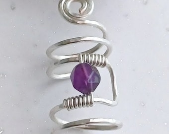 May include: A silver wire ring with a purple gemstone. The ring is made of multiple coils of wire, with a small gemstone in the centre.