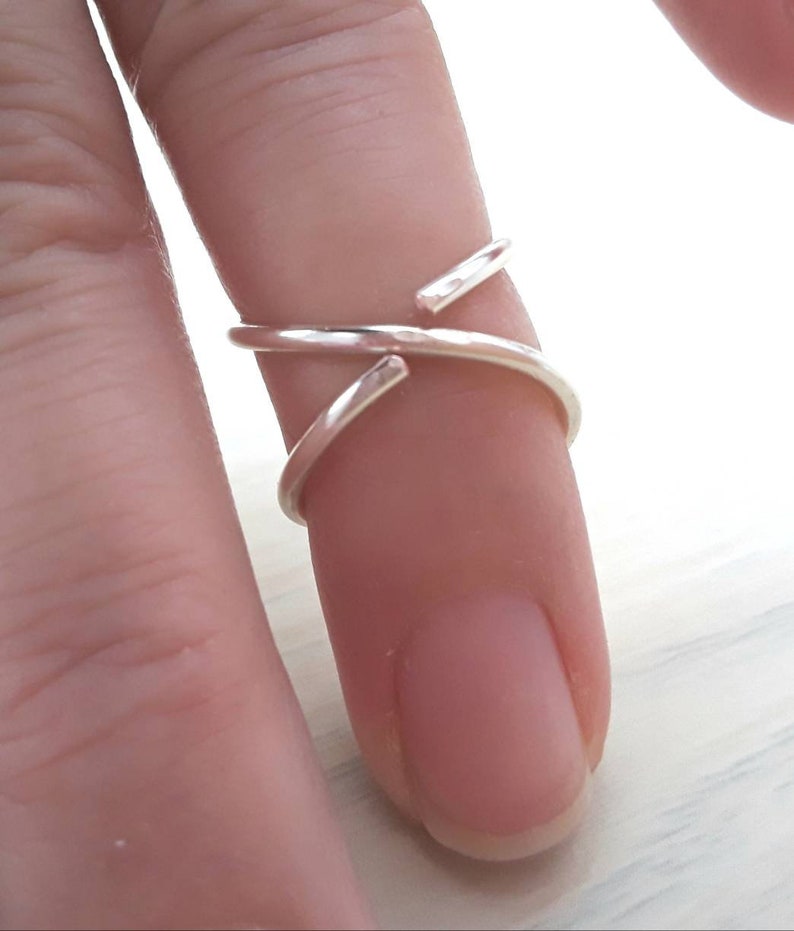 Puede incluir: Un anillo de plata con un dise&ntilde;o de cruz. El anillo se lleva en un dedo.