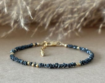 May include: A delicate bracelet featuring small, dark, rough-textured beads interspersed with tiny, smooth, polished gold-tone metal spheres. The bracelet includes a gold-tone metal lobster claw clasp and an adjustable chain link extension.