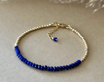 May include: A gold beaded bracelet with a section of faceted, deep blue beads. The bracelet has a delicate chain and clasp, and is displayed on a neutral surface.