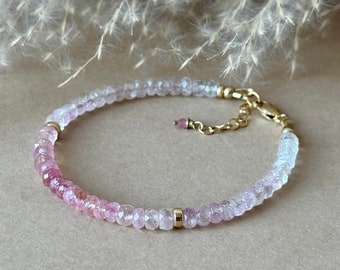 May include: A delicate bracelet featuring a gradient of pink and white gemstones. The bracelet is secured with a gold clasp and chain. The gemstones are small and round, creating a subtle, elegant accessory.
