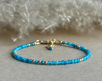 May include: A delicate bracelet featuring small, faceted bright blue beads interspersed with tiny, polished gold-toned metal spheres. The piece includes a gold-toned metal lobster claw clasp and a short extender chain with a single blue bead.