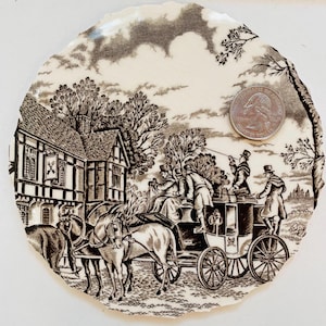 May include: A brown and white ceramic plate with a vintage design featuring a horse-drawn carriage, a building with a sign that says "The Cross Keys", and trees. The plate is approximately 6 inches in diameter.