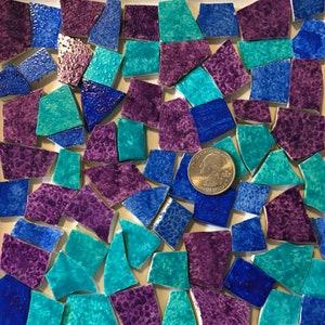 May include: A collection of small, irregular shaped ceramic tiles in shades of teal, blue, and purple. The tiles are arranged in a random pattern and are approximately the size of a US quarter.