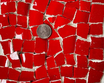 May include: A collection of irregularly shaped, bright red ceramic pieces with white undersides, arranged on a white surface. A US quarter coin is placed among the pieces for size comparison. The pieces vary in size and shape.