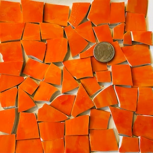 May include: A collection of orange mosaic tiles, some of which are irregular in shape, arranged on a white surface. A US quarter is included for scale.