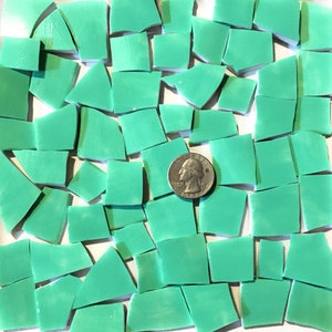 Puede incluir: Una colección de azulejos de mosaico verde turquesa, algunos cuadrados y otros de formas irregulares, con una moneda de 20 céntimos de euro para la escala.