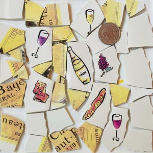 May include: A collection of broken ceramic pieces featuring wine-related illustrations. The fragments depict wine glasses, bottles labeled "MACON", grapes, and a baguette. Some pieces have yellow and beige text.