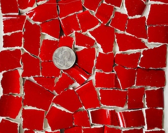 May include: A collection of red ceramic tile shards with white edges, scattered on a white surface. A US quarter coin is placed among the shards for size comparison. The tiles are irregularly shaped and have a glossy finish.