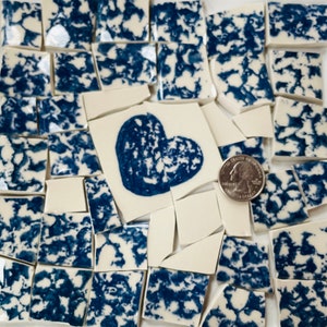 May include: A collection of blue and white ceramic mosaic tiles with a heart shape in the center. The tiles are broken into irregular shapes and sizes. A US quarter is included for scale.