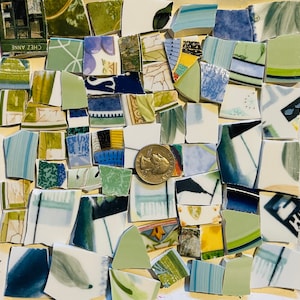 May include: A collection of broken ceramic pieces in various shapes and sizes, featuring shades of green, blue, white, and yellow. Some pieces have floral or abstract patterns. A coin is included for scale. The image includes a small piece of paper with the text "Chez Anne".