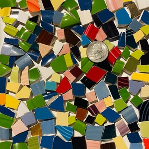 May include: A close-up of a mosaic made of small, colorful ceramic tiles. The tiles are arranged in a random pattern and include shades of red, green, blue, yellow, and white. A silver coin with the inscription "Liberty" is visible in the center of the mosaic.