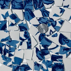 May include: A collection of blue and white ceramic mosaic tiles with a floral pattern. The tiles are broken into irregular shapes and sizes, and a US quarter is included for scale.