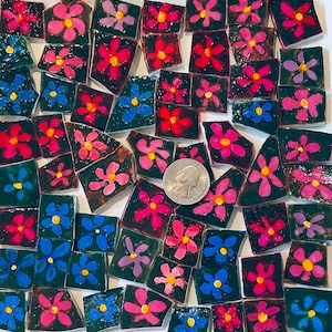 Könnte beinhalten: Eine Sammlung bunter Mosaikfliesen mit rosa, roten und blauen Blumendesigns auf schwarzem Hintergrund. Die Fliesen sind in einem zufälligen Muster angeordnet und eignen sich perfekt für Bastelprojekte.