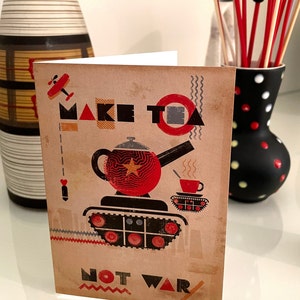 Pode incluir: Cartão com design vintage. O cartão apresenta uma chaleira vermelha num tanque, uma chávena de chá e as palavras "MAKE TEA NOT WAR". O cartão tem um aspeto envelhecido e desgastado.