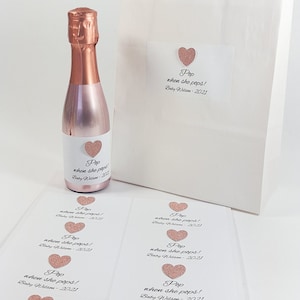 May include: A set of 8 pink and white favour tags with the text "Pop when she pops! Baby Wilson - 2021" and a pink glitter heart. The tags are designed for a baby shower.