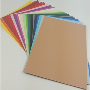 May include: A selection of coloured cardstock paper fanned out to display a range of hues. The colours include red, orange, yellow, green, blue, and purple. A large tan sheet of paper is in the foreground.