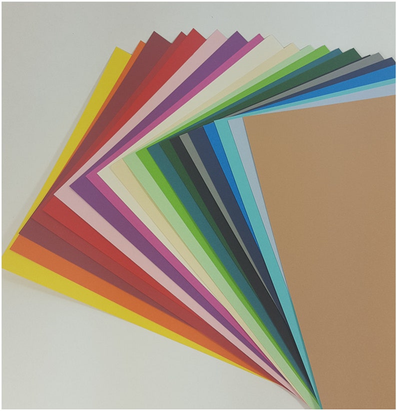 May include: A selection of coloured cardstock paper fanned out to display a range of hues. The palette includes yellow, red, purple, green, and blue. The paper is arranged in a layered pattern, suitable for crafts and stationery.