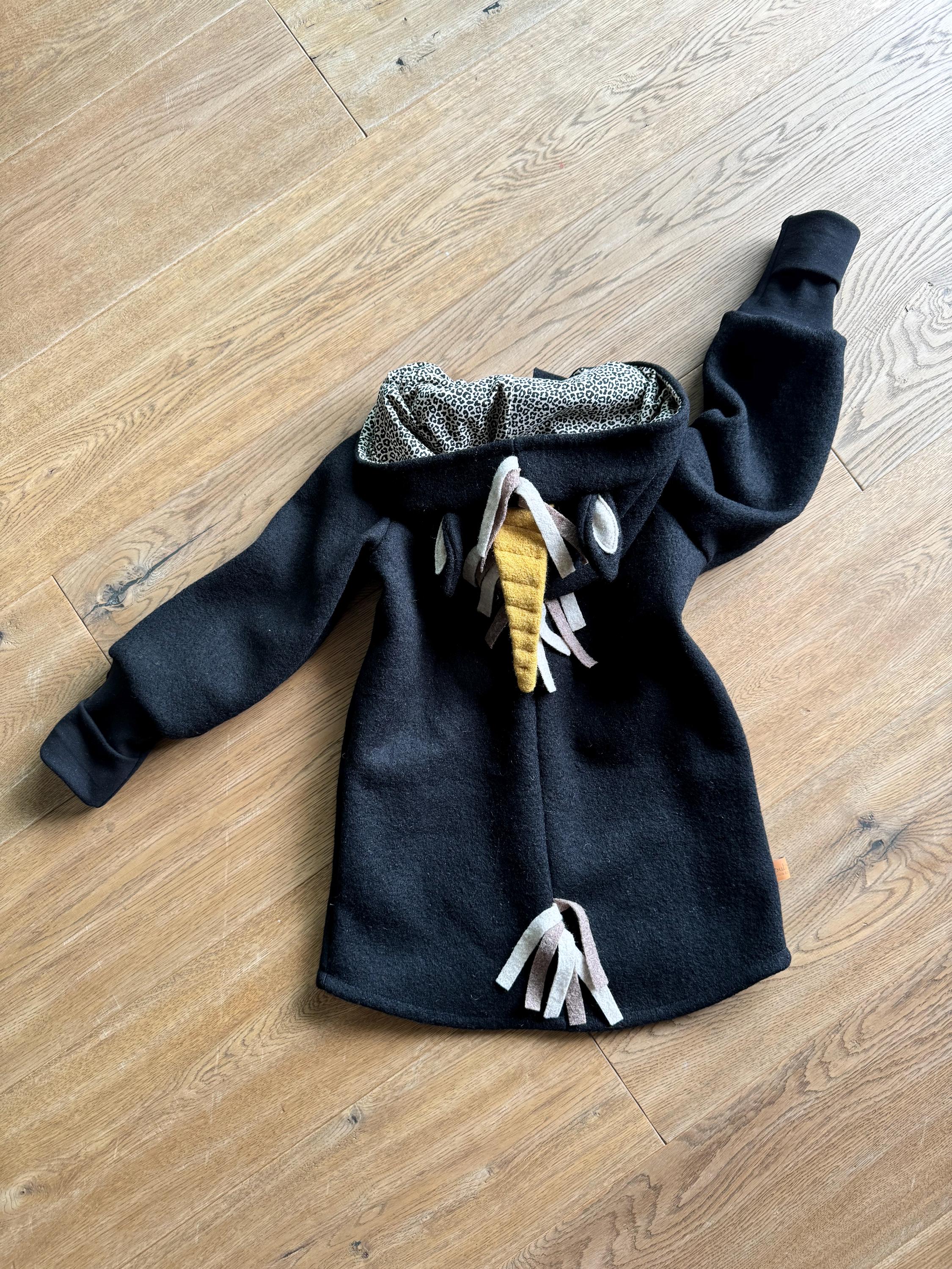 Puede incluir: Sudadera con capucha negra con un dise&ntilde;o de unicornio. La capucha tiene un forro estampado en blanco y negro. El unicornio tiene un cuerno amarillo y borlas marrones y beige.