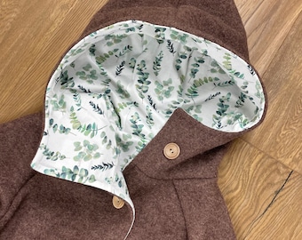 May include: A brown hooded jacket with a white lining featuring a green leaf pattern. The jacket has wooden buttons.