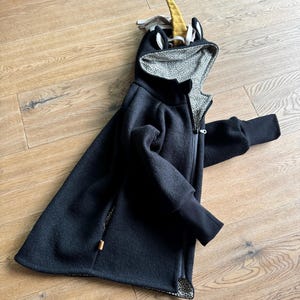 Puede incluir: Una chaqueta negra con capucha con un dise&ntilde;o de unicornio en la capucha. La capucha est&aacute; forrada con un estampado de animal negro y blanco.