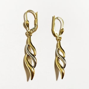 May include: A pair of gold and silver dangle earrings with a twisted, flame-like design. The earrings have a lever back closure.