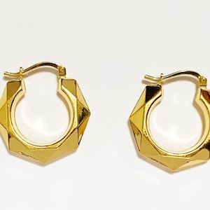 Op de afbeelding: Een paar gouden creolen met een geometrisch ontwerp. De oorbellen zijn gemaakt van glanzend metaal en hebben een licht afgeronde vorm.