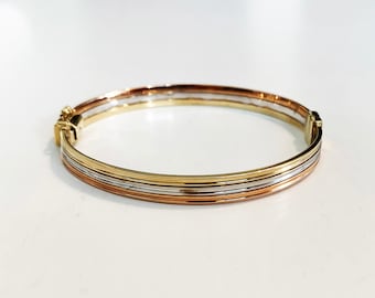 May include: A gold bangle bracelet with three bands of different colored gold: yellow, white, and rose.