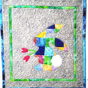 May include: A patchwork bunny with a white tail, surrounded by green and blue floral designs, on a gray background.