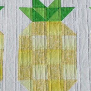 Puede incluir: Camino de mesa acolchado con un dise&ntilde;o de pi&ntilde;a repetido. Cada pi&ntilde;a est&aacute; hecha de tela de cuadros amarillos con hojas verdes, sobre un fondo blanco. Los bordes est&aacute;n acabados con un borde verde oscuro.