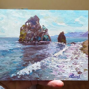 May include: A painting of a seascape with two rocky islands in the distance. The water is a deep blue and the sky is a light blue with white clouds. The painting is done in a loose, impressionistic style.