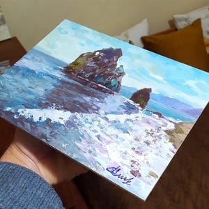 May include: A painting of a seascape with two rocky islands in the foreground. The water is a deep blue with white foam crashing against the rocks. The sky is a light blue with white clouds. The painting is signed "Chust" in the lower right corner.