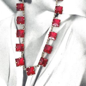 May include: A red glass bead necklace with a silver chain. The necklace features square-shaped beads with a faceted design.
