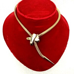 May include: A gold-toned snake chain necklace with a knotted pendant. The pendant is made of two pieces of metal that are intertwined.