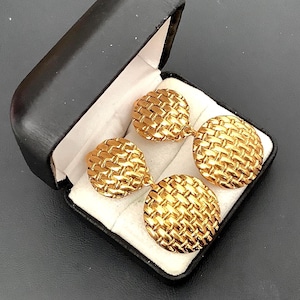 May include: Gold-coloured cufflinks with a basketweave pattern, displayed in a black box with a white lining. The cufflinks are circular and have a polished finish, possibly vintage or classic in style.